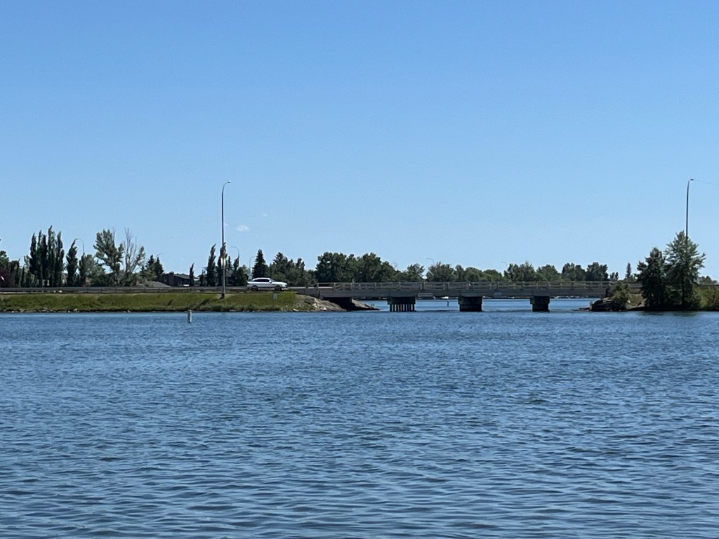 A bridge over the water that you can paddle under when on the late. There is a car about to cross the bridge. 